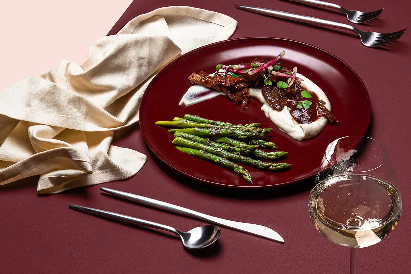 A plated seitan dinner with asparagus and white wine on a burgundy table